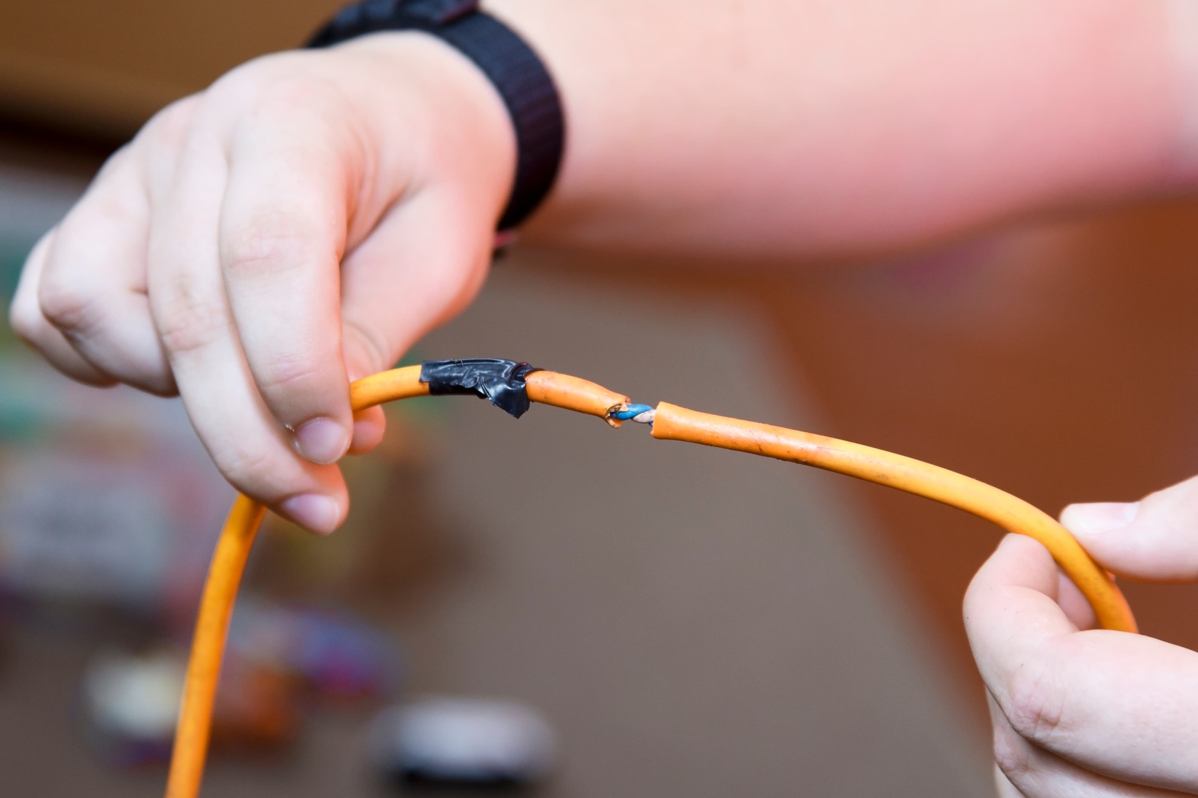 Close-up of a damaged electrical cord being held by a professional, highlighting the importance of regular PAT testing to ensure electrical safety and prevent accidents.