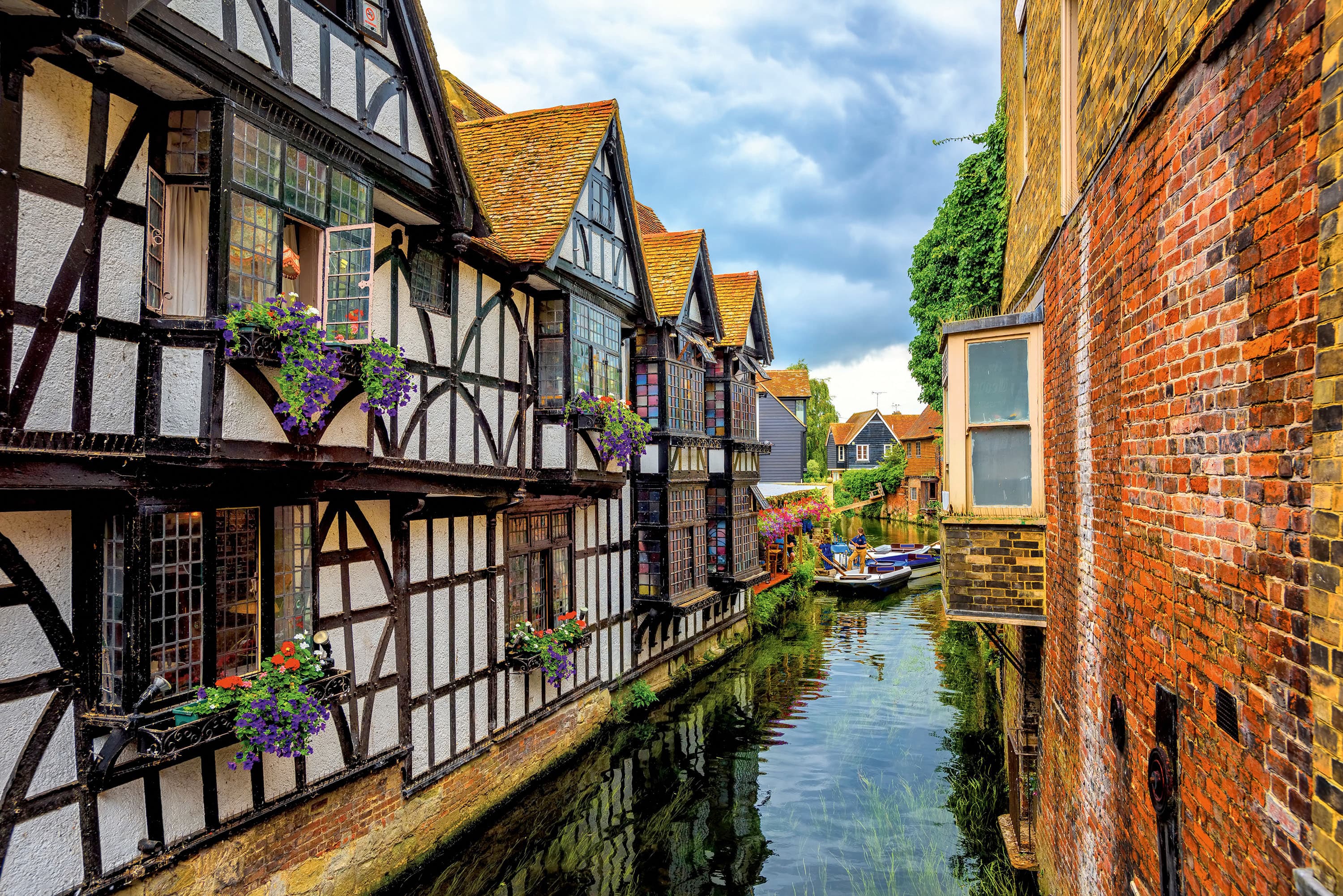 Charming canal in Canterbury, Kent, featuring picturesque Tudor-style houses with timber frames and flower boxes. A serene waterway scene showcasing the historic and architectural beauty of Canterbury, a popular destination in the UK.