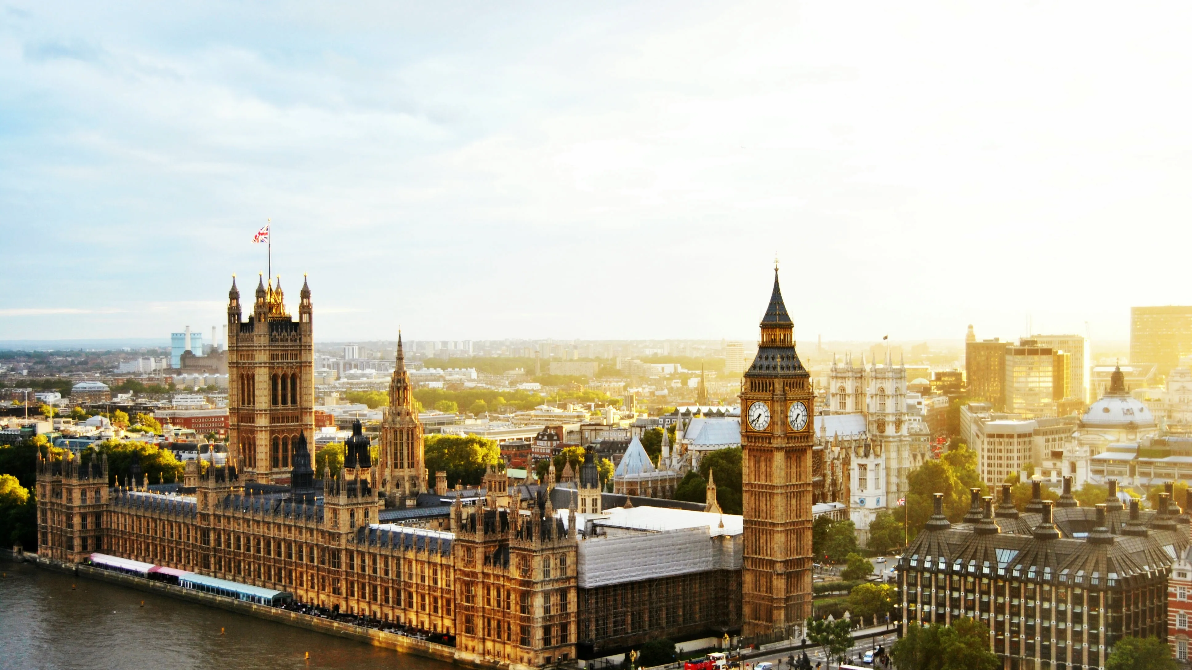 Panoramic view of Westminster Palace and Big Ben in London at sunset, highlighting iconic Gothic architecture and the Thames River.